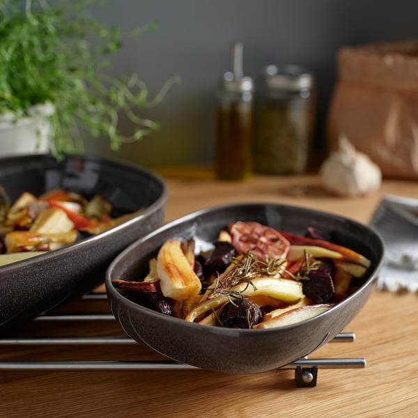 Two dark grey GLADELIG dishes with roasted food on a metallic trivet.
