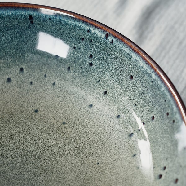 Close-up of a teal, stoneware plate with speckled glaze and brown trim.