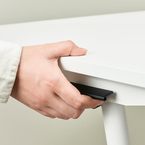 A person adjusts a sit-stand desk, pinching a handle to smoothly raise the tabletop.
