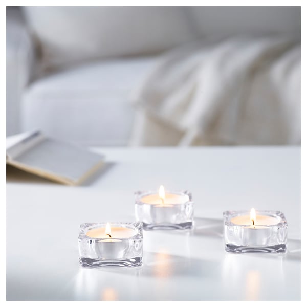 Three lit tea lights in clear glass holders on a white surface, creating a cosy atmosphere.