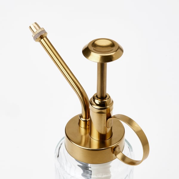 Gold-colored metal plant mister with long tube atop clear glass bottle, stylish & functional.
