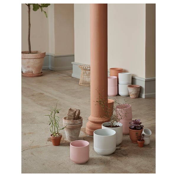 Colourful, stacked plant pots in soft hues--pink, blue, white--with vertical grooves, arranged around a column. Different shapes and sizes, indoors.