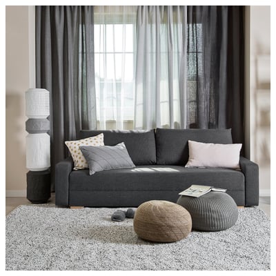 Modern grey sofa-bed with colourful pillows, round pouffes, and tall white lamp.