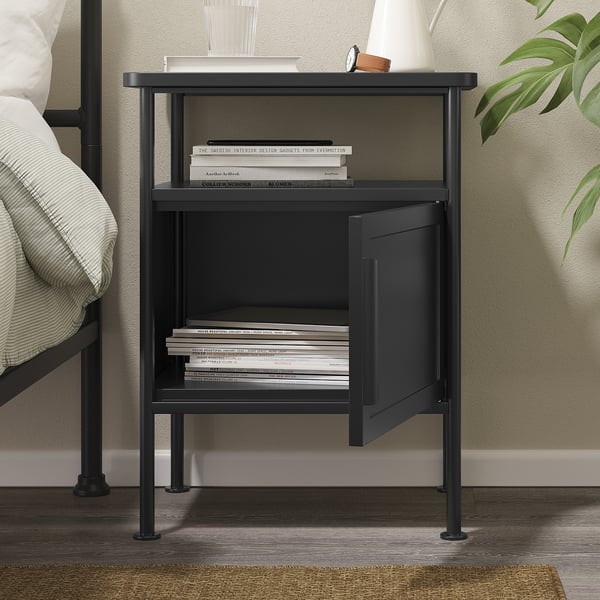 Black bedside table with open shelf, closed cabinet, and adjustable feet. Stores books and hides clutter.