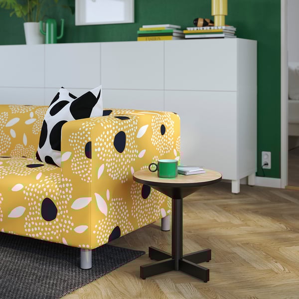 Yellow patterned couch with spots, black side table, green mug, book.