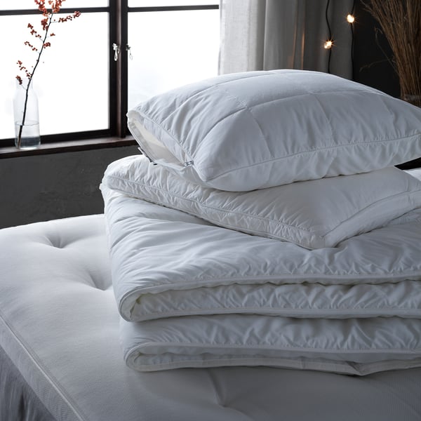 White GRÖNAMARANT pillow on bed, featuring supportive core, fluffy outer filling, and double piping for enhanced support.
