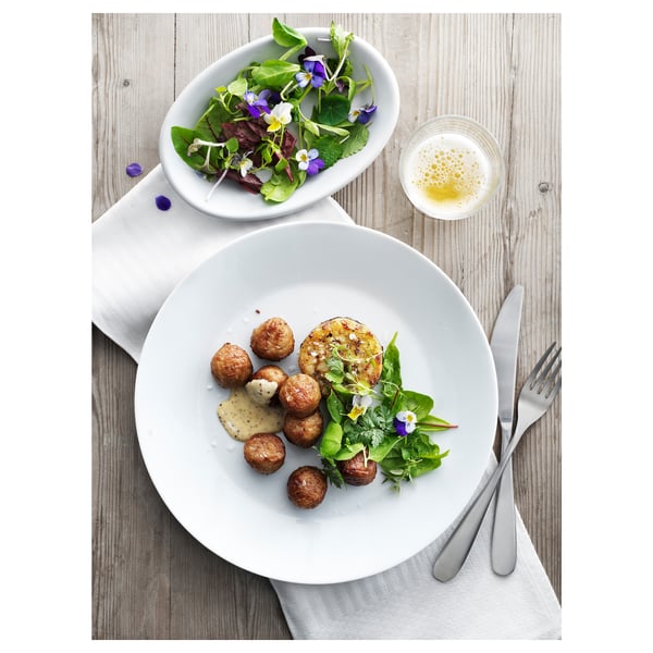 A gourmet dish displayed on rustic wood: crispy croquettes, greens, and dipping sauce in white bowls.
