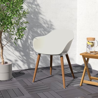 Modern outdoor scene: white GRÖNSTA chair with wooden legs by a small table holding a drink, near a large plant against a light wall.