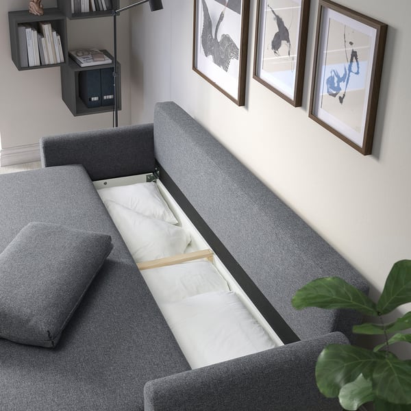 Modern grey sofa with bed pulled out, showing storage and wall art.