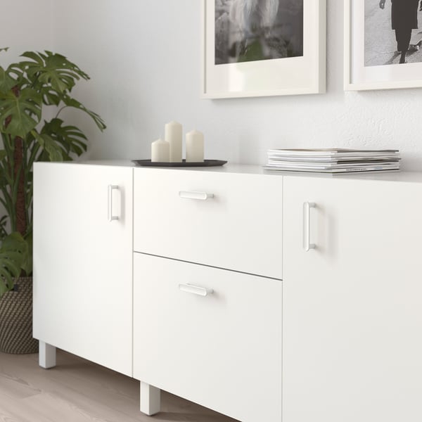 White cabinet with three drawers and two doors, adorned with candles and plant, offering storage and decorative space.