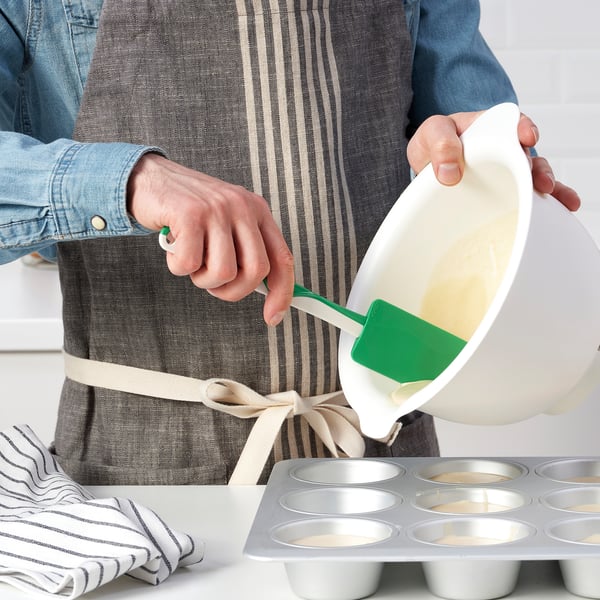Person pours batter into muffin tin using a green spatula.