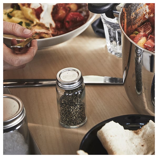 Small glass jar of black pepper on kitchen counter, used for seasoning during cooking.