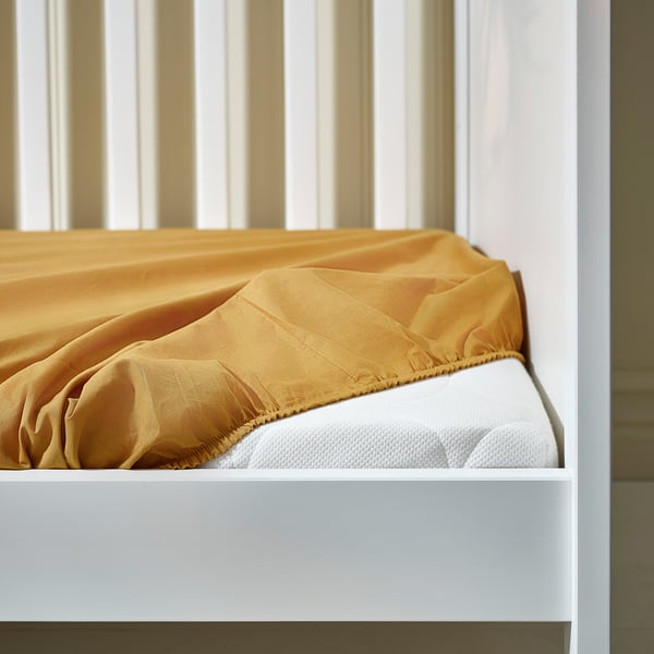 A crib mattress with a yellow fitted sheet, secured with elastic, ensuring a safe and comfortable sleep for a baby.
