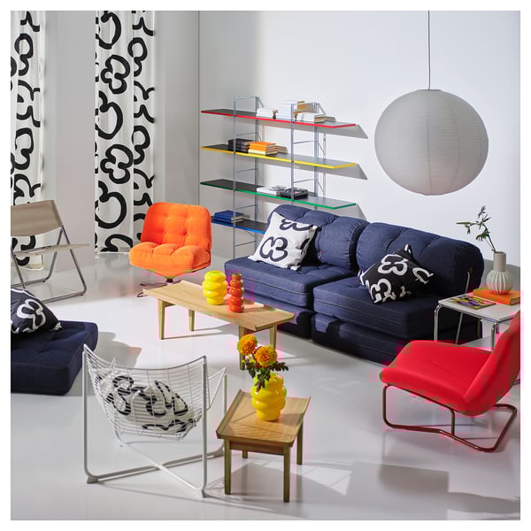 Modern living room with GULLSUDARE pendant lamp, blue sofa, colourful chairs, wooden coffee table, large curtains, and glass shelving.