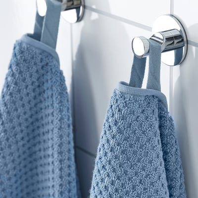 Two light blue towels hang neatly on shiny metal hooks. The soft, fluffy texture suggests absorbency and comfort, ideal for bathroom use.