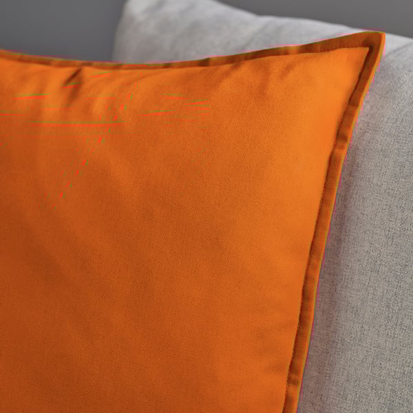 Bright orange cushion cover, smooth texture, high-quality fabric, neatly stitched edges, part of a cosy couch setting.