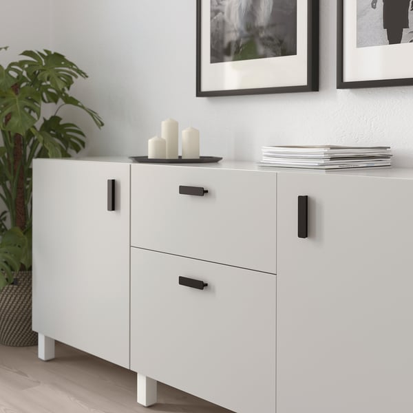White cabinet with black handles, smoothly finished. Top holds candles, bottom has drawers.