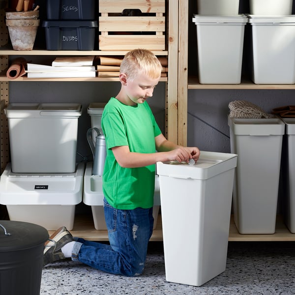Boy sorts waste into recycling bin in storage room.