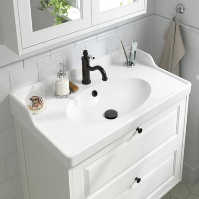 White bathroom sink with black tap and lever, aerator, soap dispenser, toothbrush holder.