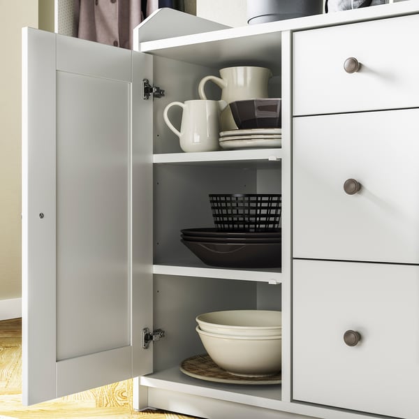 White HAUGA cabinet with open doors, showing stacked mugs, plates, and bowls on shelves.