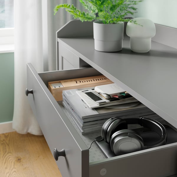 Grey HAUGA drawer with open compartment, holding books, headphones, notebooks, and stationery items.