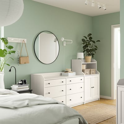Modern bedroom with HAUGA series furniture, white drawers, and cabinets, round mirror, plant, and green walls.