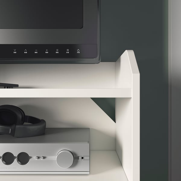 Modern white tv stand with two shelves, one with black headphones and remote controls, and another with a silver audio device.