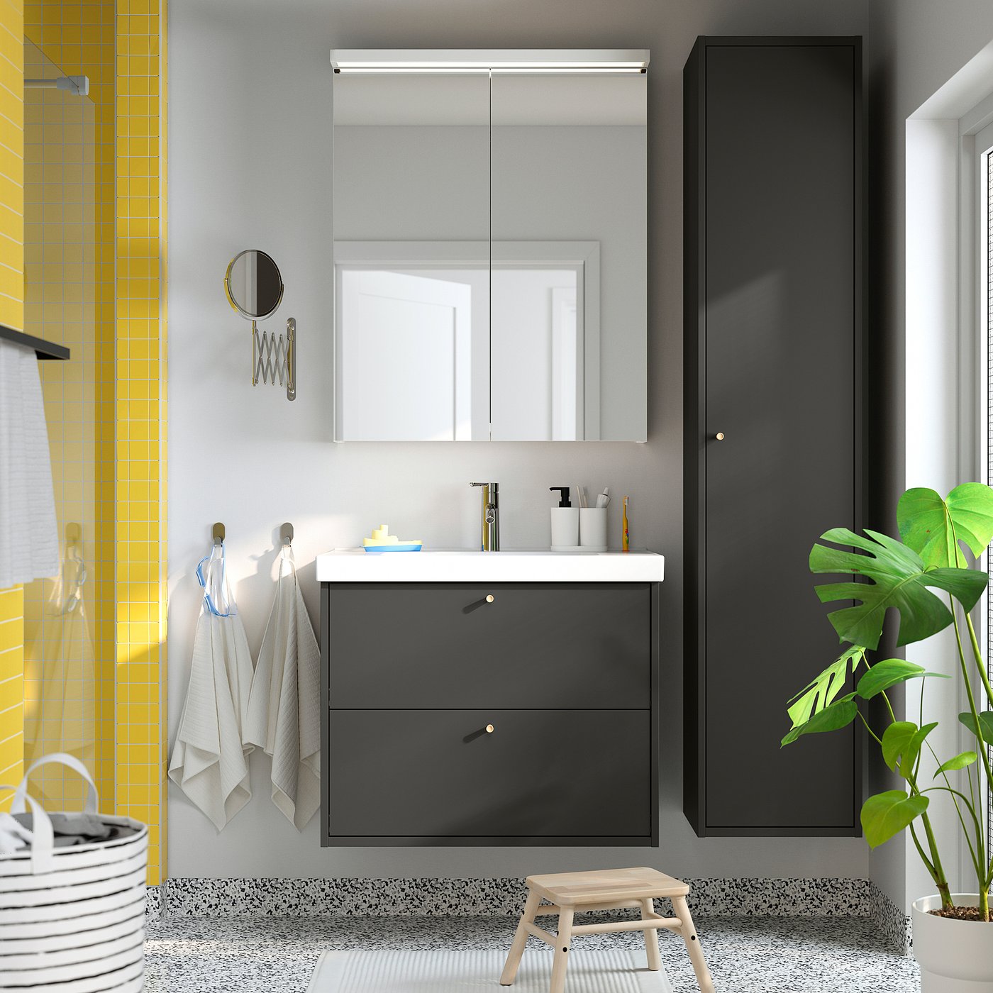 Modern bathroom with grey HAVBÄCK cabinet, mirror, towels, and plant. Tall, sleek, wall-mounted storage.