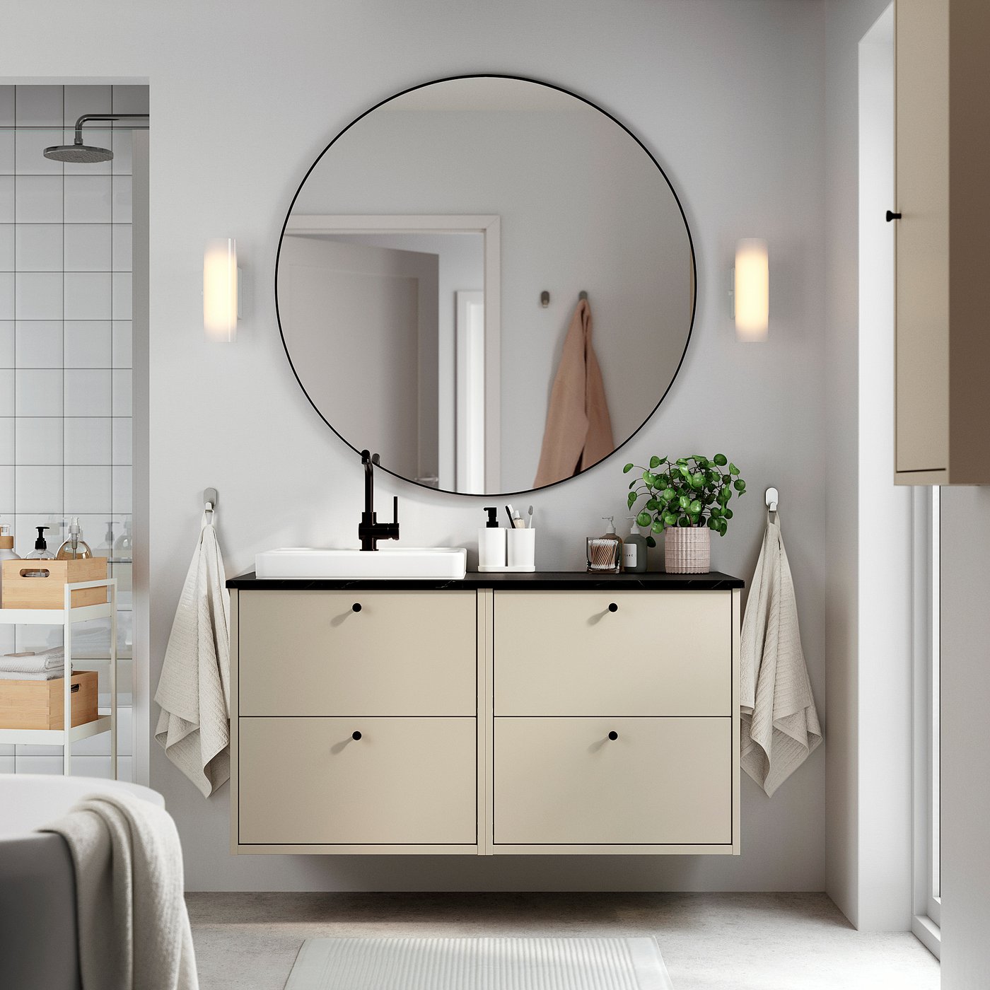 Modern bathroom with beige HAVBÄCK vanity, round mirror, white towels, and plants.