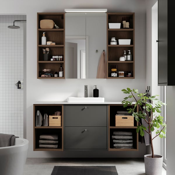 Modern bathroom with dark grey HAVBÄCK vanity, mirror, and open shelves against a white tiled wall. Includes sink and storage.