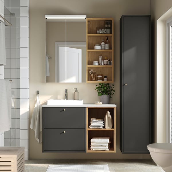 Modern bathroom with grey HAVBÄCK vanity, wooden shelves, and tall cabinet. Mirror and sink set above.