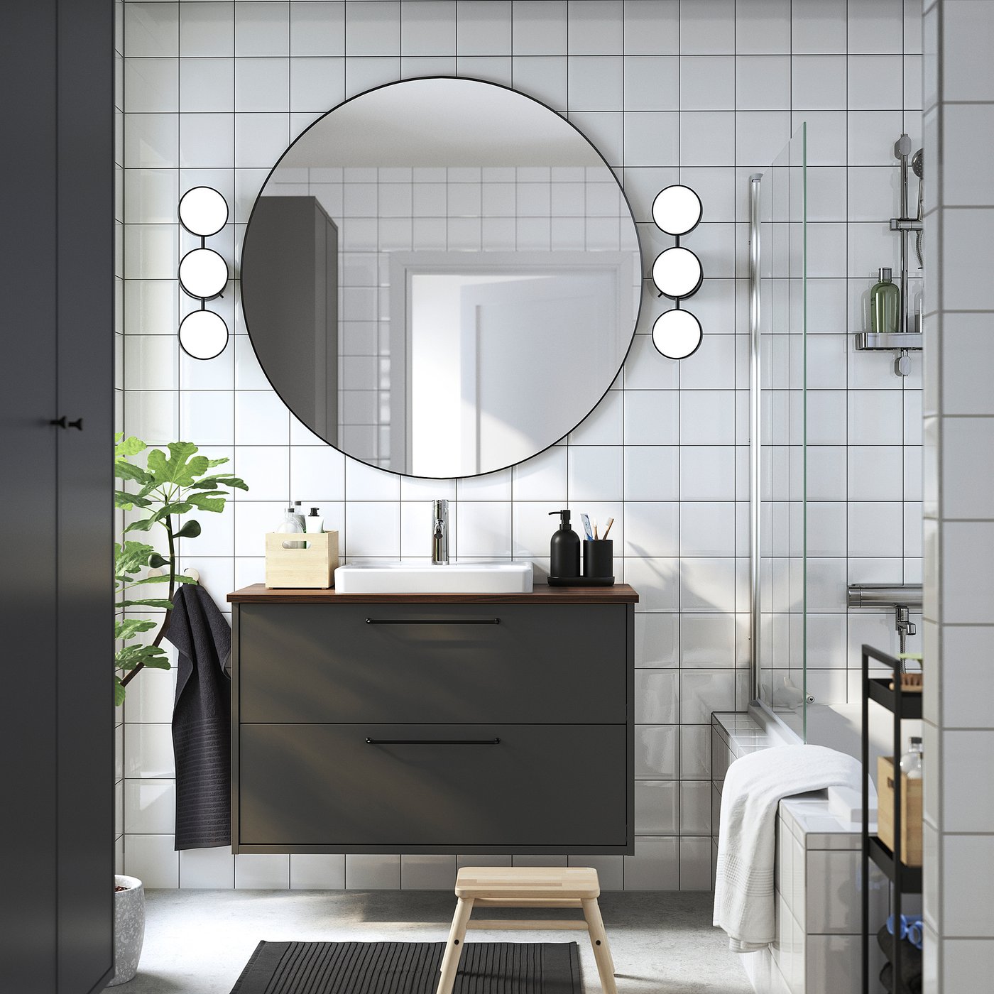 Modern bathroom with dark grey vanity, mirror, lights, stool, and glass shower.
