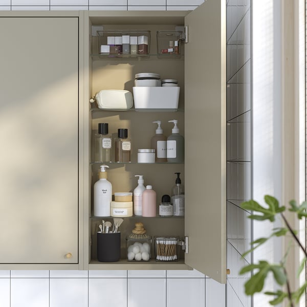 A beige wall cabinet with glass shelves, storing various toiletries like bottles, jars, and brushes. Hinged dampers close the door silently.
