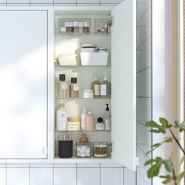 Modern bathroom cabinet with glass shelves, holding various toiletries and organisers.