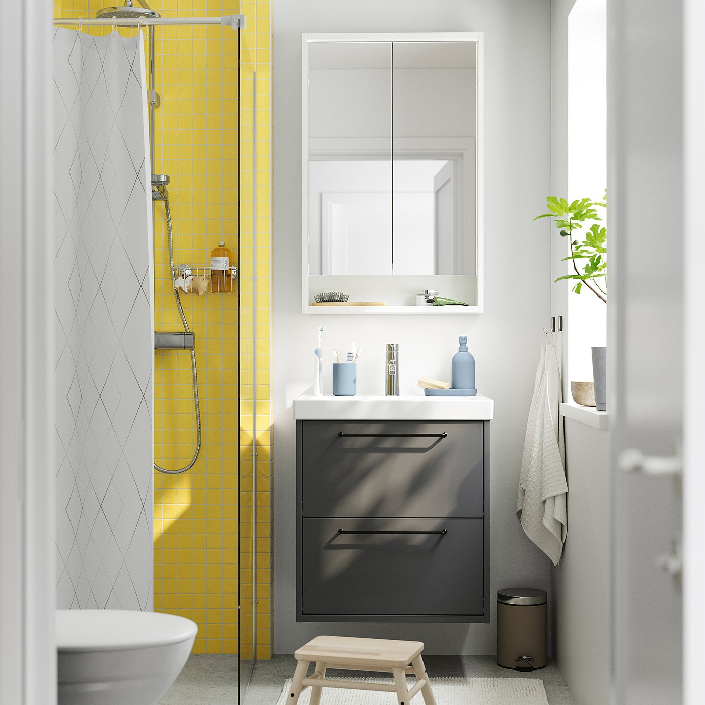 Small bathroom with dark grey HAVBÄCK vanity & yellow tiles. Cells, mirror, white sink, & plant.