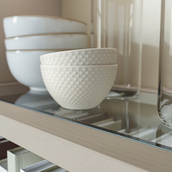 White ceramic bowl with dotted texture, on glass shelf in light wooden cabinet.