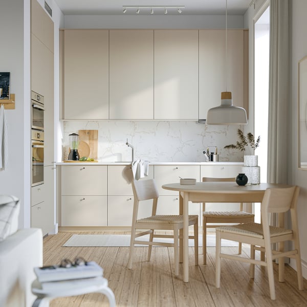 Modern kitchen with beige HAVSTORP cabinets, wooden chairs around small table, marble backsplash, and white pendant lamp.