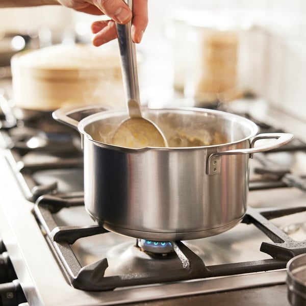 Adjusting a pots lid on a stove, steam rises, showcasing its heat-resistant glass design and built-in strainer.