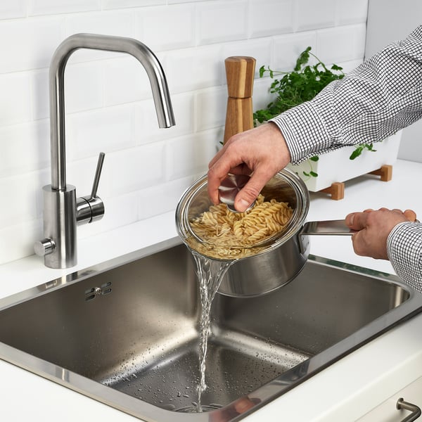 Person draining pasta in kitchen sink with modern silver tap.