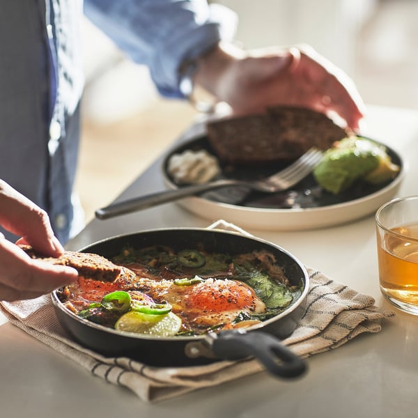 Cooking: person ladles food from non-stick pan on table.