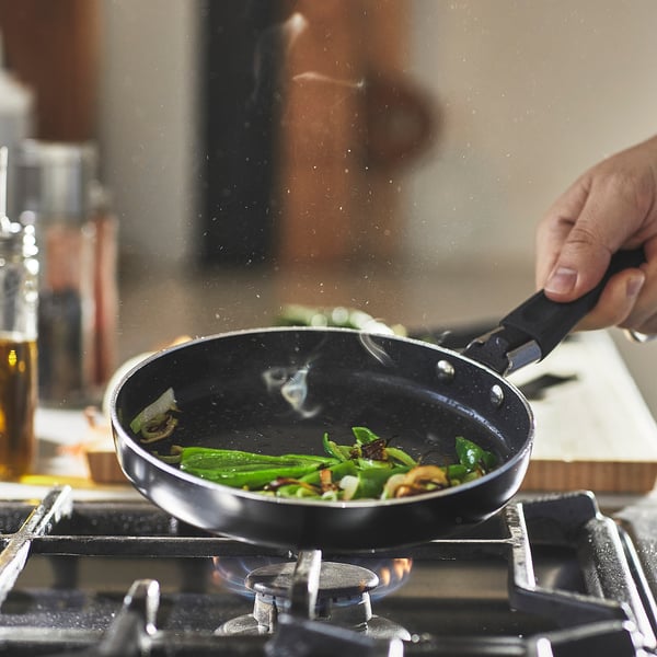 Hand stirs veggies in a small, non-stick frying pan on a gas stove.