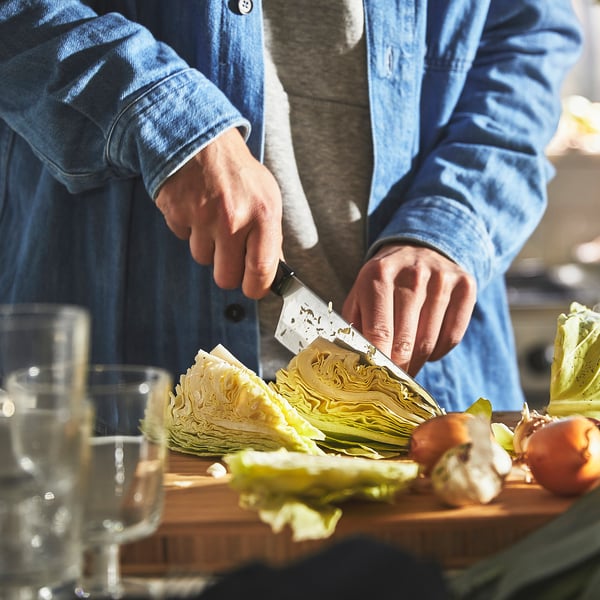 A person chops cabbage with a knife on a cutting board with other vegetables.