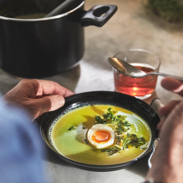 Black non-stick saucepan on table, person holding, red tea beside.
