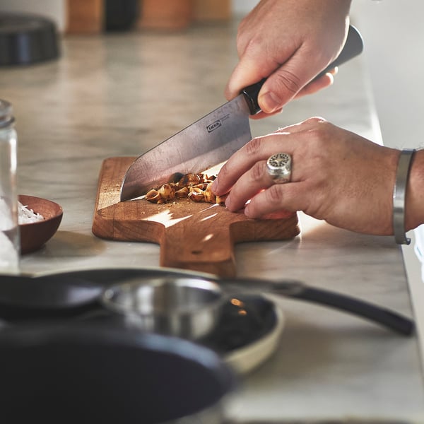 Person chopping food on a wooden cutting board using an ikea knife.