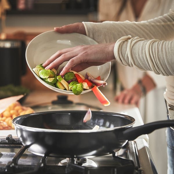 Person pours vegetables from a plate into a frying pan on a stove.