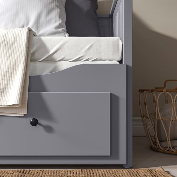 A grey HEMNES day-bed with drawers, showing a folded white bedding set on top.