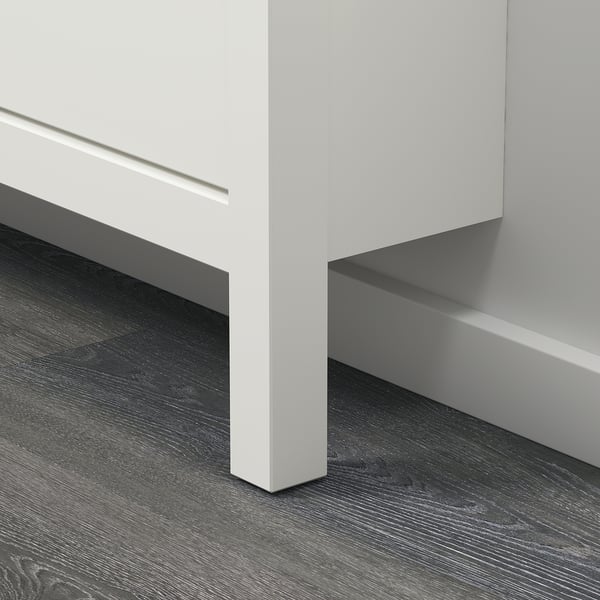 A sleek, white HEMNES shoe cabinet with a modern design. Made of durable materials, it stands against a wall with a dark wooden floor underneath.