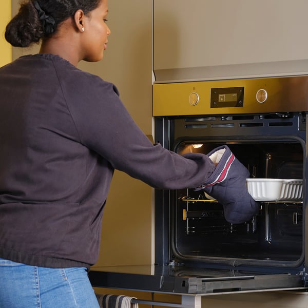 A person uses oven mitts to place a dish into a built-in oven.