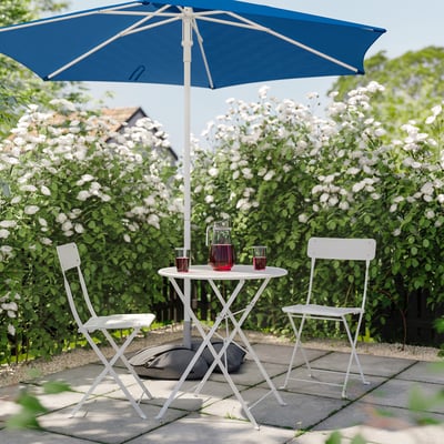 Outdoor setup with blue parasol, two white chairs, table, and flowers.