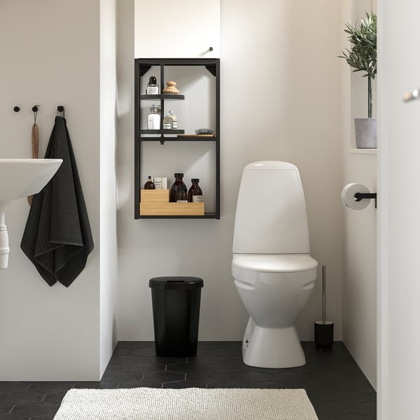 Modern bathroom: white walls, dark tiles, toilet, bin, brush, towel, shelf, plant.